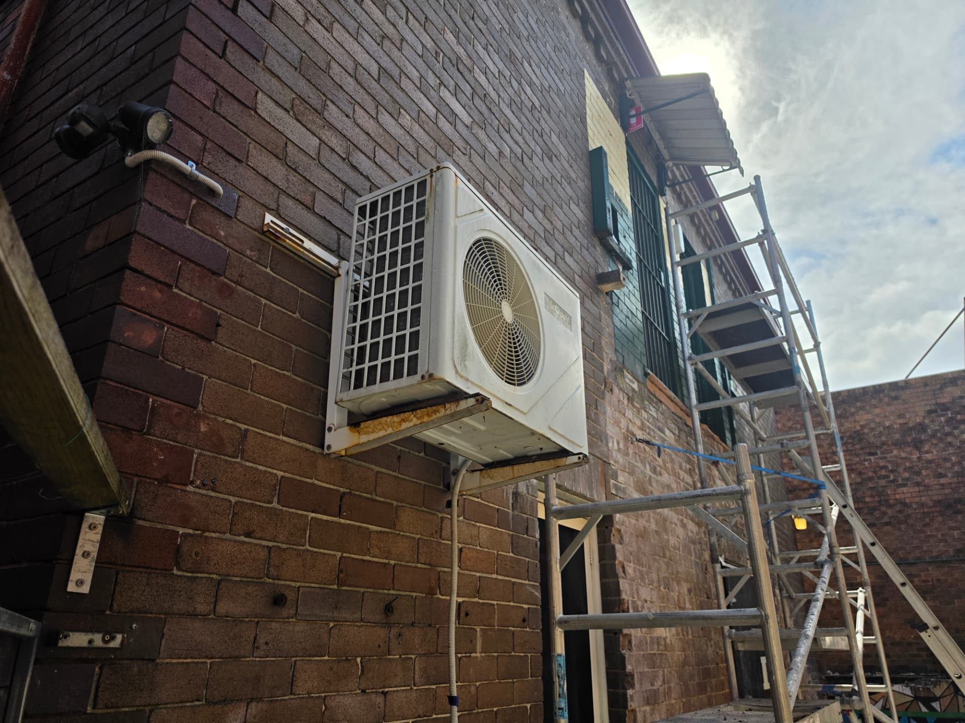 Scaffolded brickwork work area beside an external air-conditioning unit