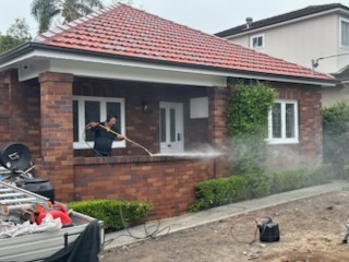 Worker pressure cleaning the front of a single-storey red brick home
