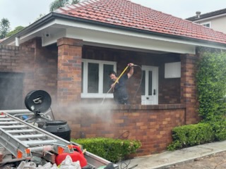 Worker pressure cleaning red brickwork beneath the front porch